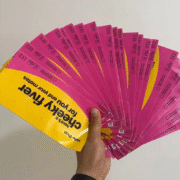 手持展开的粉色和黄色快递袋,印有Hello Zhao品牌标志和cheeky flyer字样,附有回收标志和二维码